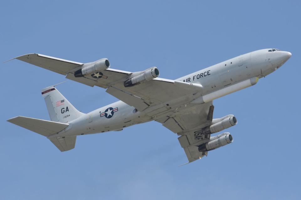 An E-8C Joint STARS aircraft flying in a lightly cloudy sky.