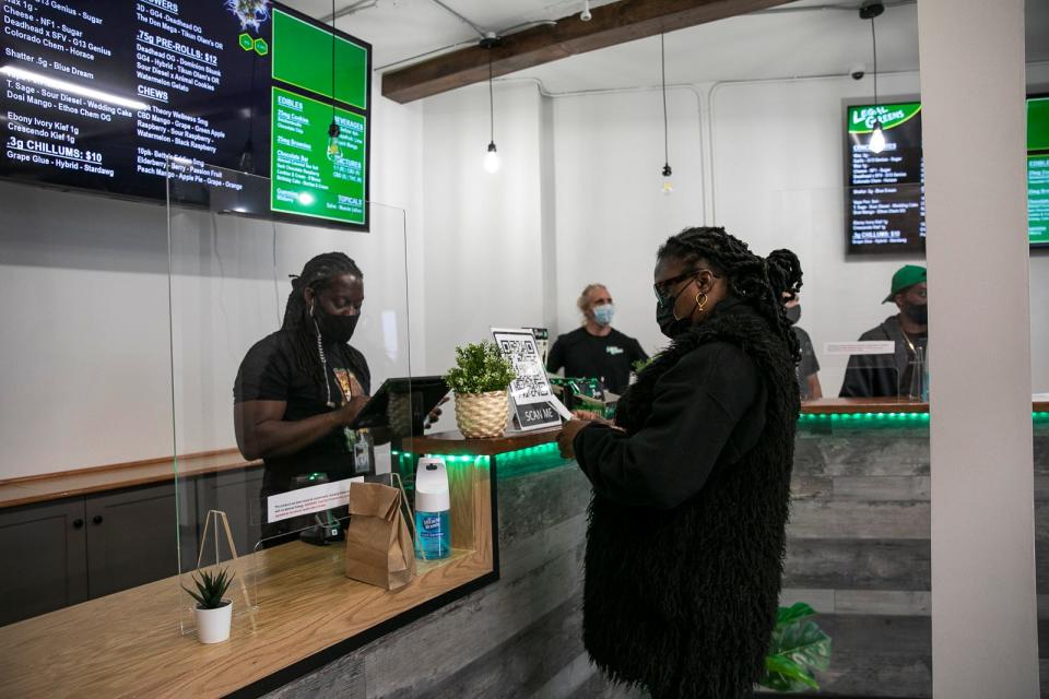 Legal Greens owner Mark Bouquet, left, assists Nicole Cola, the first customer of the Legal Greens recreational marijuana dispensary, on opening day in Brockton on Sunday, March 28, 2021.