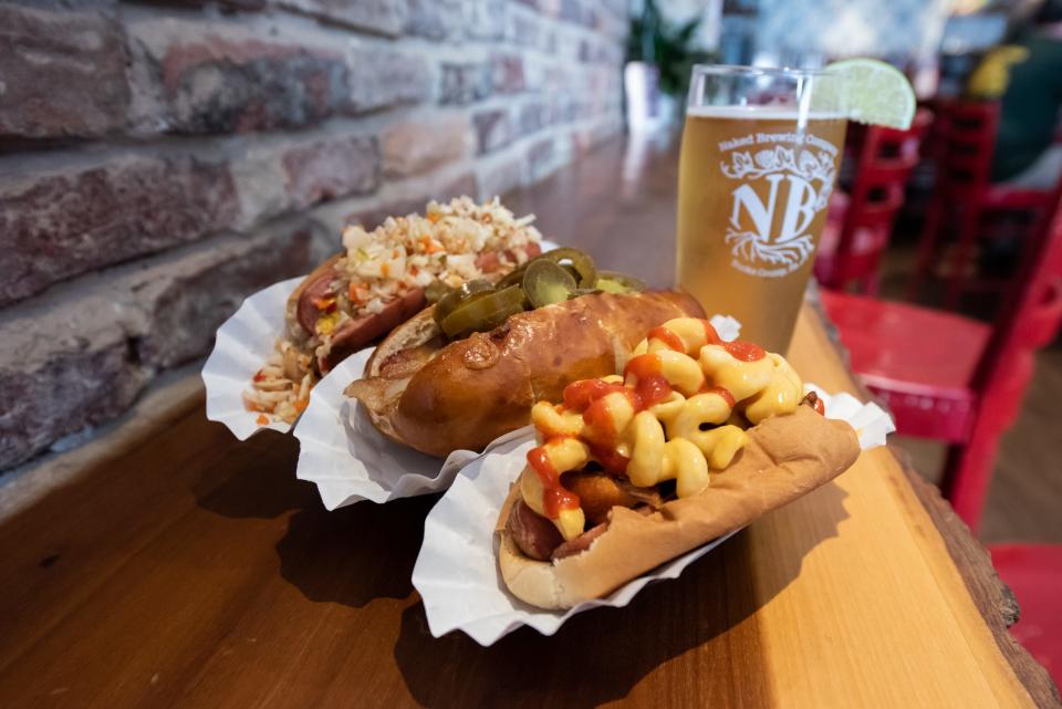 Cheese Dawgs in Bristol Borough serves dozens of uniquely topped signature and specialty hot dogs. Pictured from front to back is the Wacky Mac, Pleasant Pig and Philly Surf & Turf paired with a pint of Naked Brewing's Louie Lime lager.