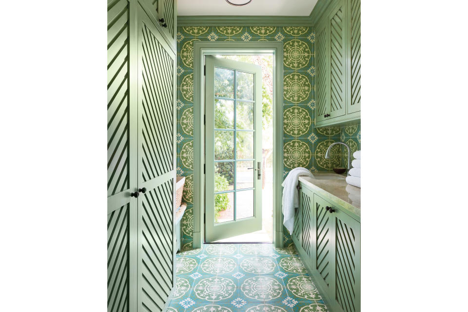 <p>Though guests enter through the more formal foyer, the homeowners typically use the back door off the laundry room. “I didn’t want them to walk into a drab old utility room every time they entered the house,” says Sharpe, who lined the walls and floors with more hand-painted tiles and dressed up the cabinetry doors with diagonal slats. “These details disguise work zones and envelop the corridor in color and a happy sense of arrival.”</p>