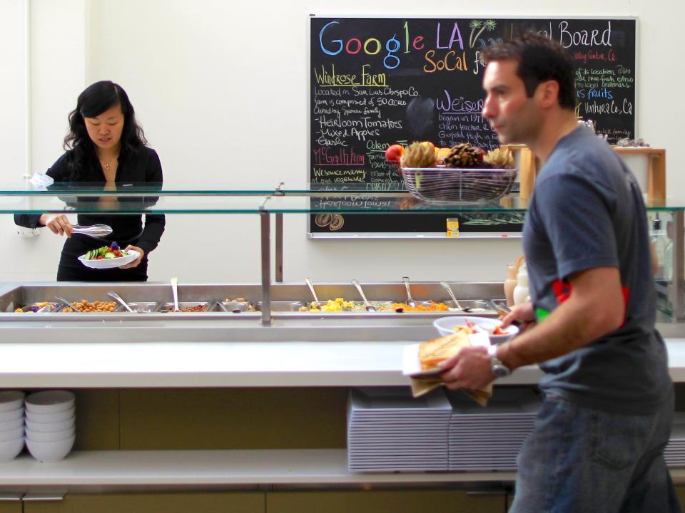 Two Google employees serving themselves lunch at one of the company&#39;s cafeterias which is stocked with fruit and salad options.