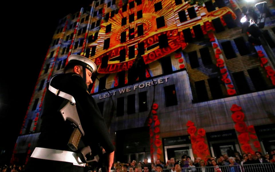 A member of the Australian Armed Forces and members of the public stand in front of a memorial message projected onto a building near the Cenotaph during the annual ANZAC Day dawn service in Sydney, Australia - Credit: DAVID GRAY/REUTERS