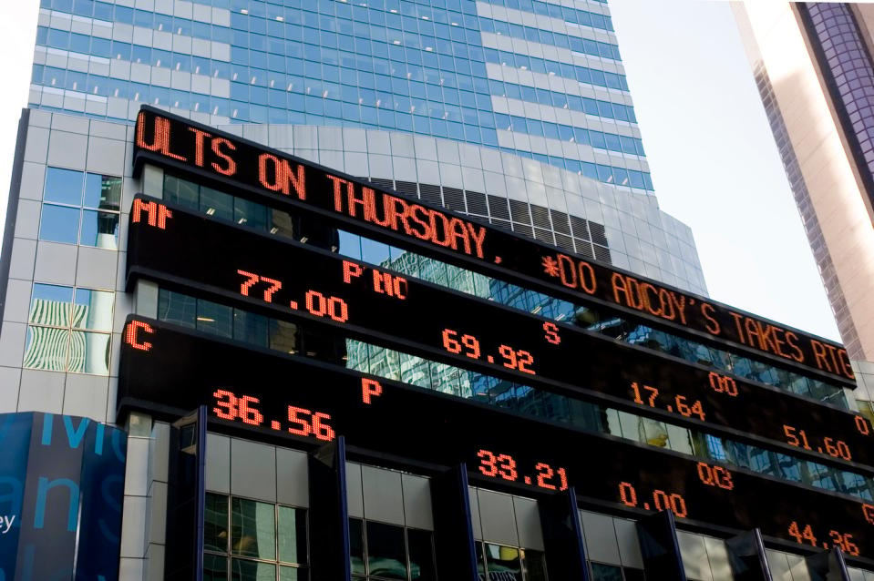 A three-tiered digital billboard displaying financial news and stock quotes on the side of a tall building.