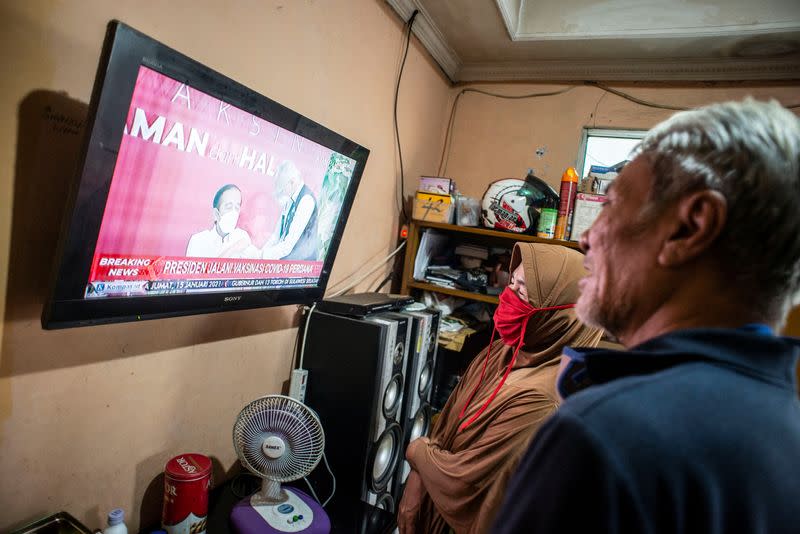 Indonesian locals watch a television showing live news of Indonesian President Joko Widodo receiving his COVID-19 vaccine shot in Jakarta, Indonesia