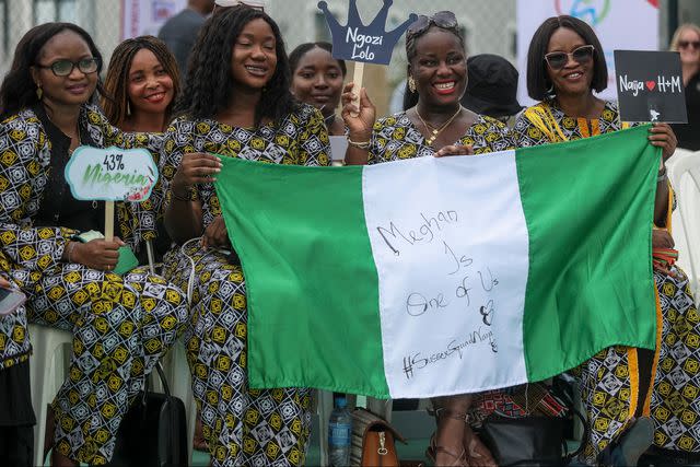 <p>KOLA SULAIMON/AFP via Getty</p> People hold up a Nigerian flag as they wait to welcome Britain's Prince Harry, Duke of Sussex, and Britain's Meghan, Duchess of Sussex, ahead of their arrival for an exhibition sitting volleyball match in Abuja on May 11, 2024