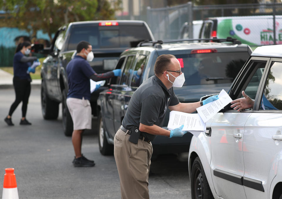 Eddie Rodriguez (right) and other Hialeah city employees hand out unemployment applications to people in their vehicles in front of the John F. Kennedy Library on April 8. (Photo: Joe Raedle/Getty Images)