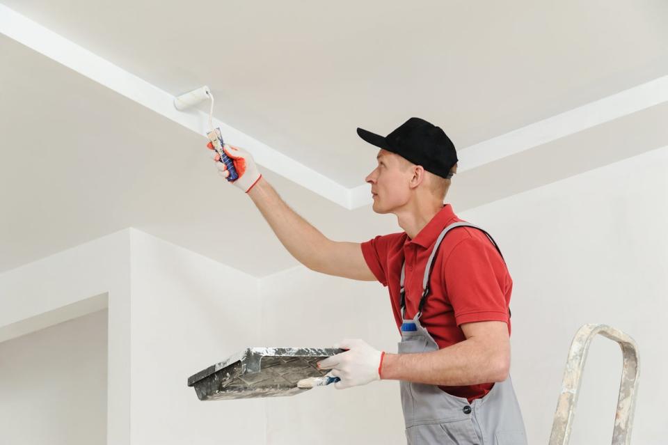 professional painter on a ladder using a small roller to paint the ceiling