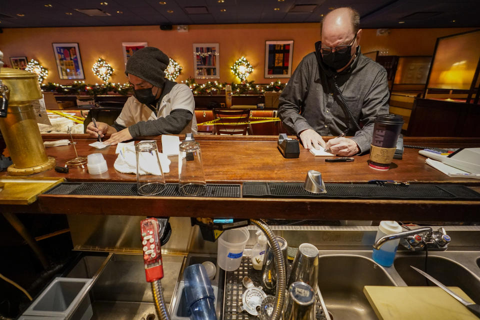 Steve Olsen, right, owner of the West Bank Café and Segundo Agueza take to-go orders over the phone in the empty restaurant, Saturday, Jan. 9, 2021, in the Hell's Kitchen neighborhood of New York. The boarded-up windows and For Rent signs are all over the place in Manhattan’s Hell’s Kitchen neighborhood. Nearby, the Broadway theaters are all dark. But the economic darkness brought on by the coronavirus pandemic has had a few bright spots. A couple of well-loved venues have gotten financial boosts, thanks to online fundraising campaigns and even a telethon. (AP Photo/Mary Altaffer)