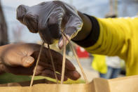 In this March 29, 2020, photo, Regina Summers hands out hot meals donated by Clydes Restaurant Group and distributed by volunteers coordinating with Martha's Table in southeast Washington. Neighborhood deliveries are part of a new Martha's Table initiative, along with community partners, to get needed food directly to the neighborhoods they serve. These volunteers are the tip of the spear for a grassroots community effort to keep Washington's most vulnerable neighborhoods fed during the unprecedented coronavirus crisis which has nearly shut down the American economy. (AP Photo/Jacquelyn Martin)