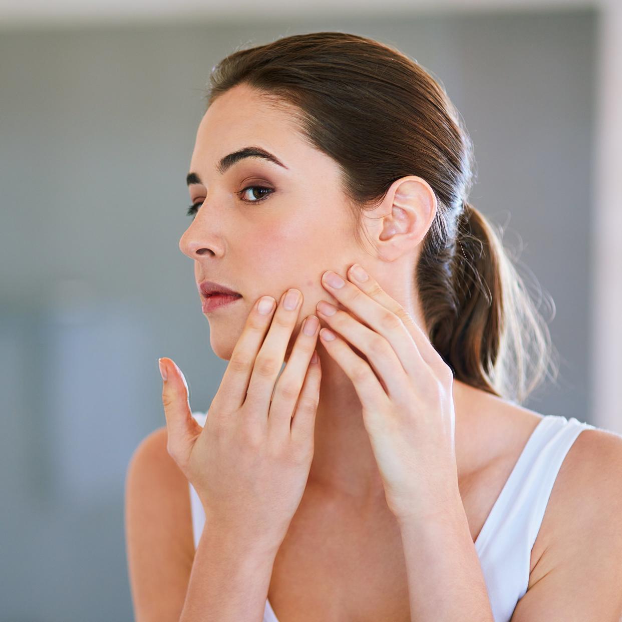 woman looking at pimple in bathroom mirror