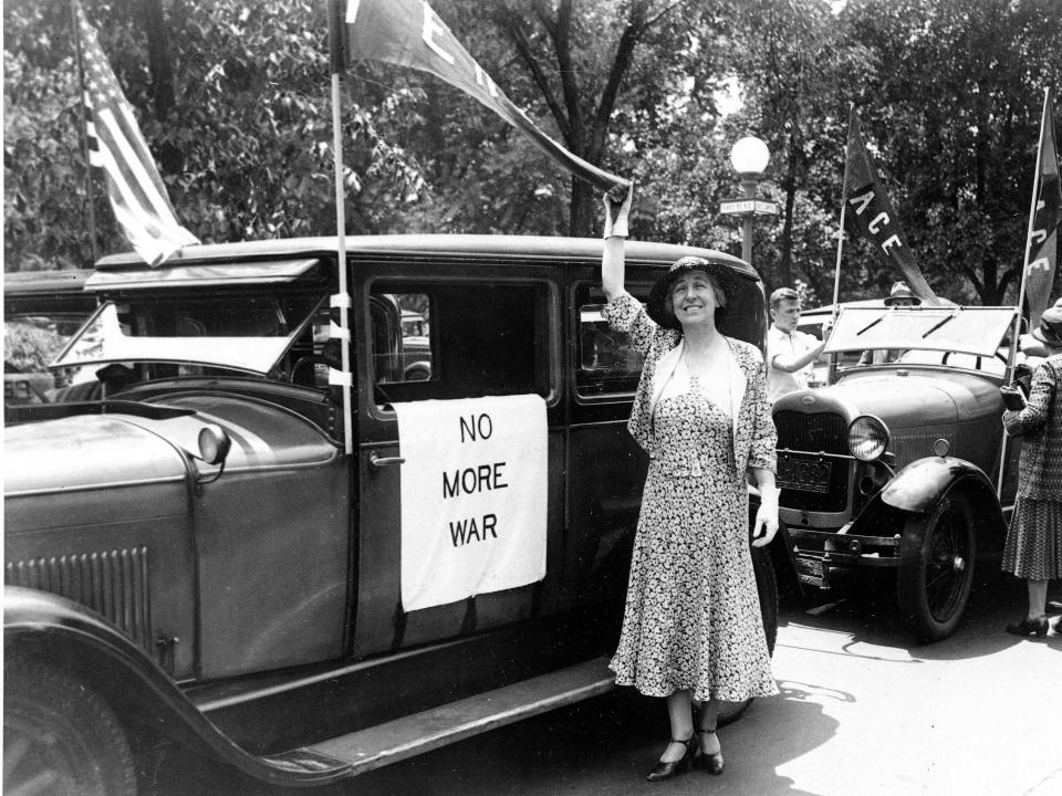 Jeannette Rankin poses by a car with a sign reading "No more war"