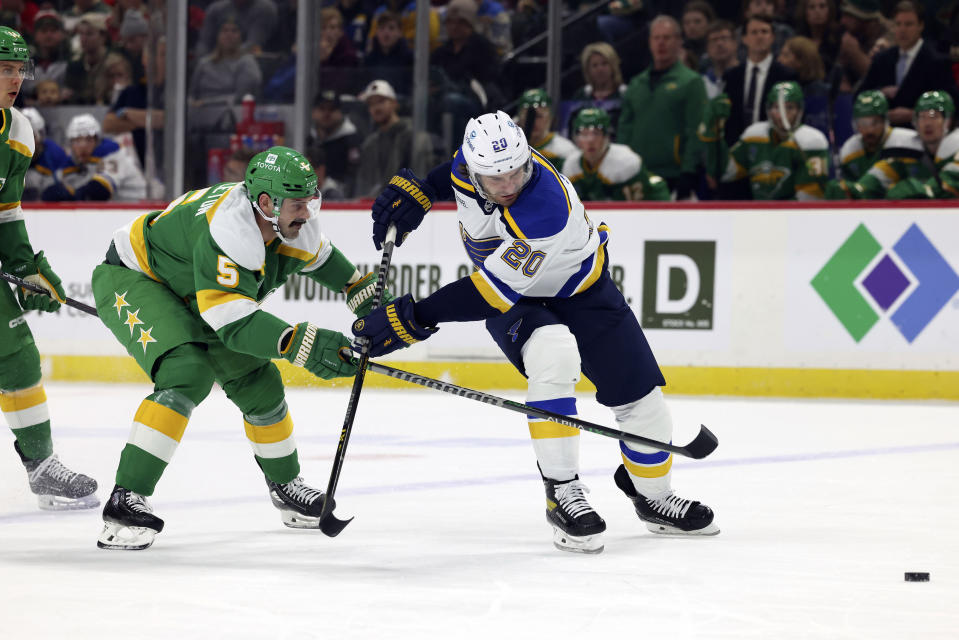 Minnesota Wild defenseman Jake Middleton (5) and St. Louis Blues left wing Brandon Saad (20) go after the puck during the first period of an NHL hockey game Sunday, Jan. 8, 2023, in St. Paul, Minn. (AP Photo/Stacy Bengs)