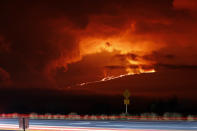 In this long camera exposure, cars drive down Saddle Road as Mauna Loa erupts in the distance, Monday, Nov. 28, 2022, near Hilo, Hawaii. Mauna Loa, the world's largest active volcano erupted Monday for the first time in 38 years. (AP Photo/Marco Garcia)