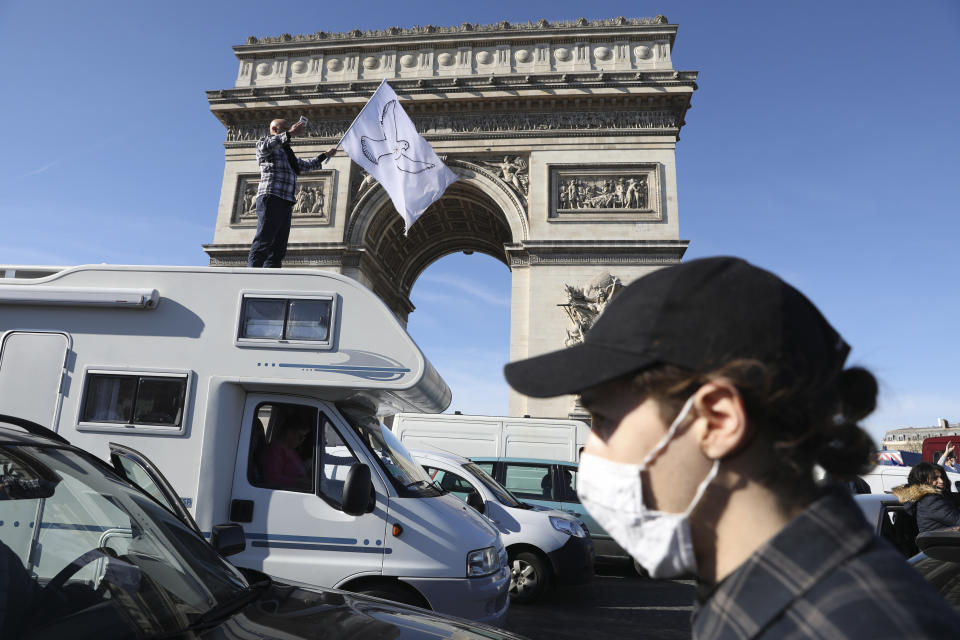 A protester stands atop a camper van as the convoy drives past the Arc de Triomphe on the Champs-Elysees avenue, Saturday, Feb.12, 2022 in Paris. Paris police intercepted at least 500 vehicles attempting to enter the French capital in defiance of a police order to take part in protests against virus restrictions inspired by the Canada's horn-honking "Freedom Convoy." . (AP Photo/Adrienne Surprenant)