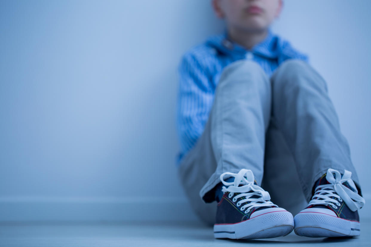 Sad boy in sneakers with asperger's syndrome sits alone in his room