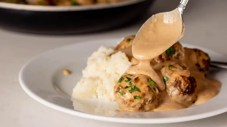 Spooning creamy sauce on meatballs and mash