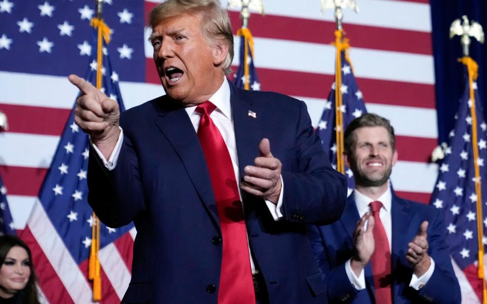 Donald Trump speaks at a caucus event flanked by his son Eric