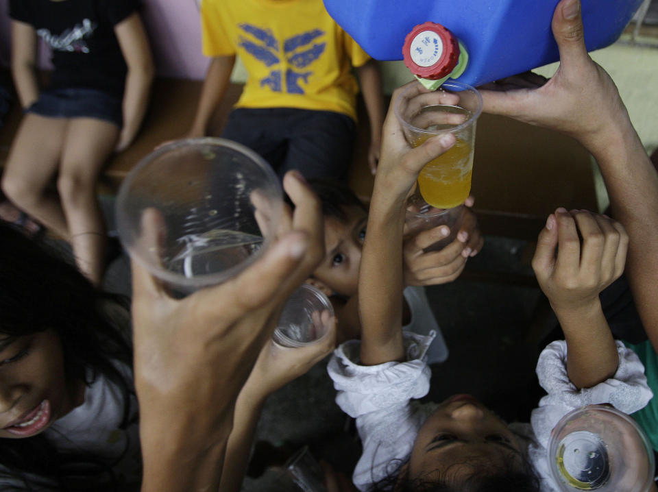 Young evacuees raise plastic cups close to a container to get the last drops of orange juice from private donors at a school that was converted into a temporary evacuation center in suburban Marikina city, east of Manila, Philippines, Friday Aug. 10, 2012. About 2.4 million people in Manila and nearby provinces have been affected, forcing more than 360,000 to seek shelter in government-run evacuation centers, the Office of Civil Defense reported Friday. (AP Photo/Aaron Favila)