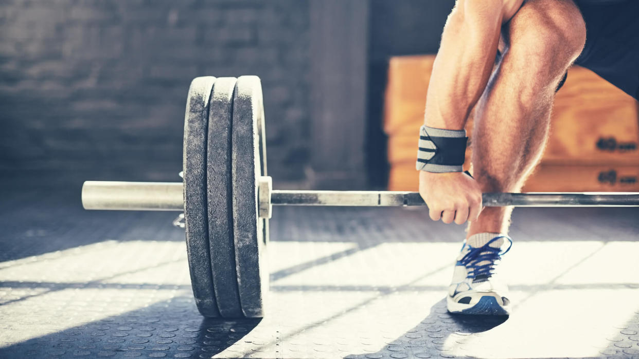 Cropped image of muscular man deadlifting barbell.