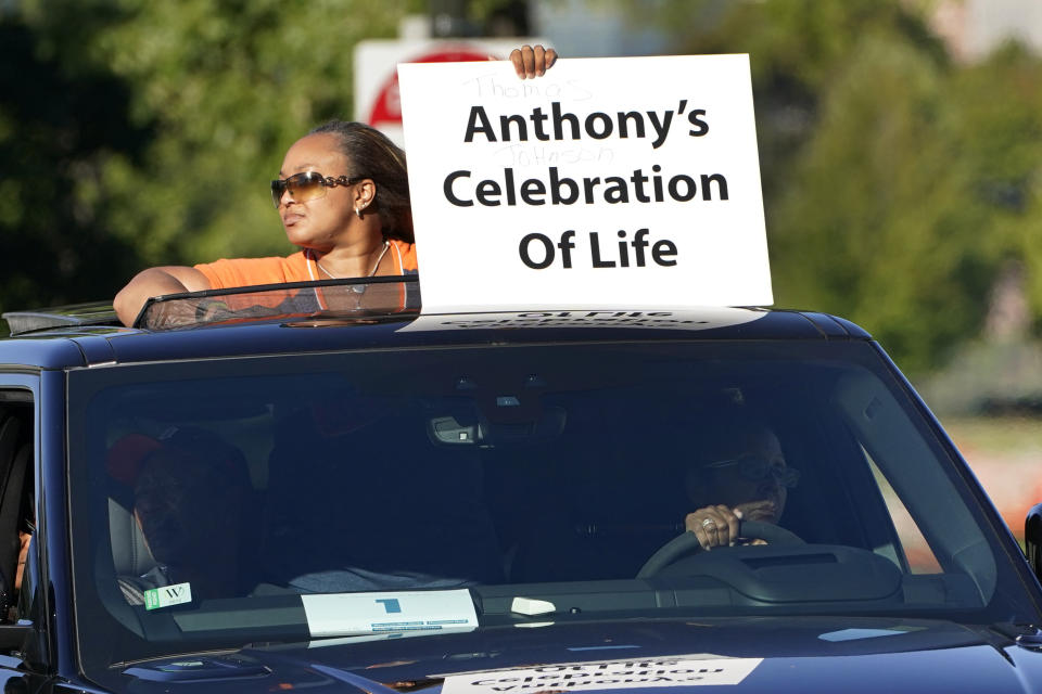 A family member holds a sign during a procession of vehicles driving past photos of Detroit victims of COVID-19, Monday, Aug. 31, 2020 on Belle Isle in Detroit. Families have a chance to take one last public look at their lost loved ones in the nation's first citywide memorial to honor victims of the pandemic. Mourners will join 14 consecutive funeral processions to drive past nearly 900 large poster-sized photos of their loved ones staked around the island. (AP Photo/Carlos Osorio)