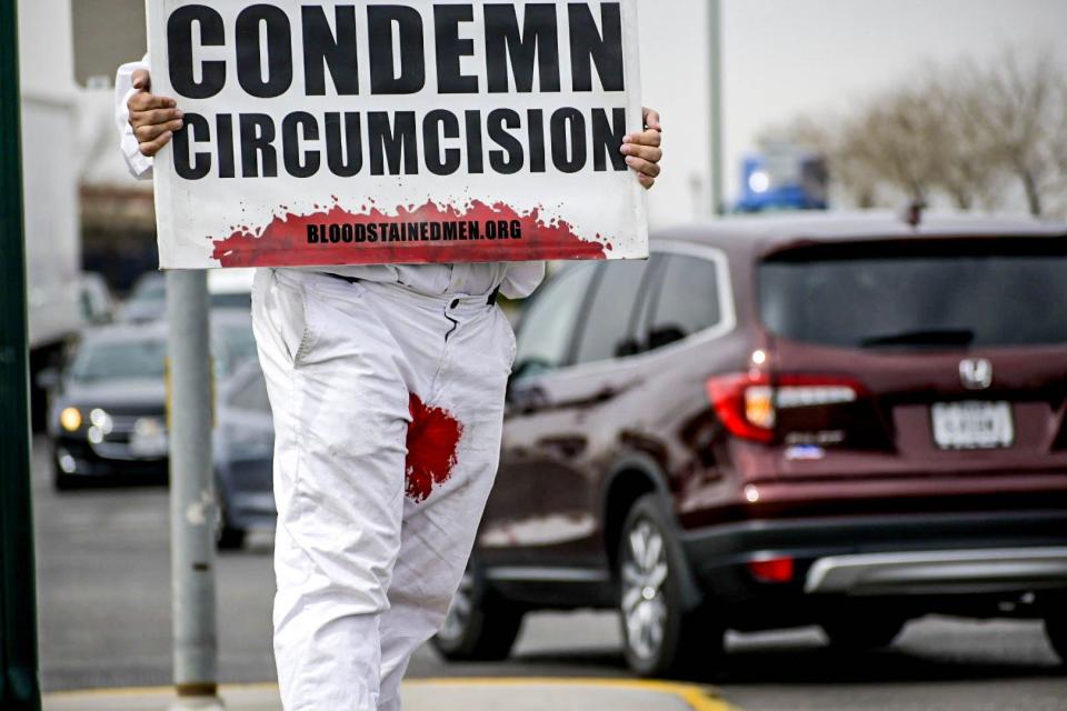 A member of anti-circumcision group, Bloodstained Men, hold a sign toward oncoming traffic on El Paso's East Side, Thursday, March. 3.