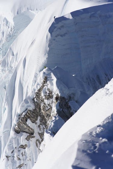 A climber looking tiny on a huge, broken ridge of snow and rock