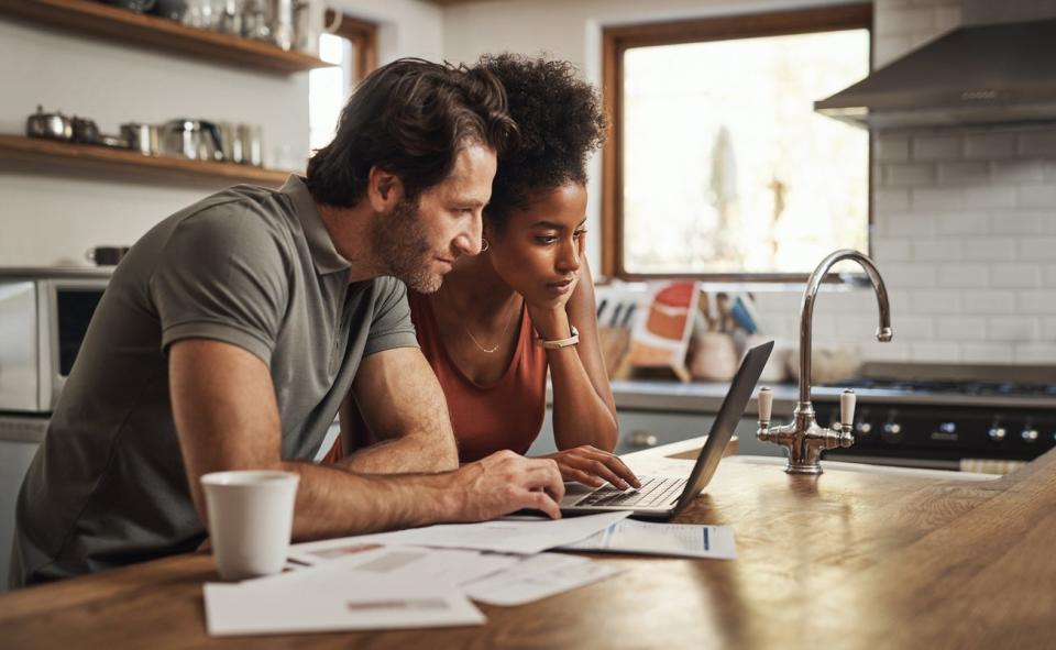 A young couple sits in kitchen doing taxes on a laptop. 