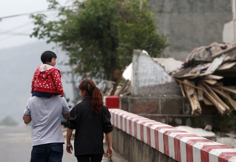 Local residents walk past damaged houses in Longmen on April 21, 2013