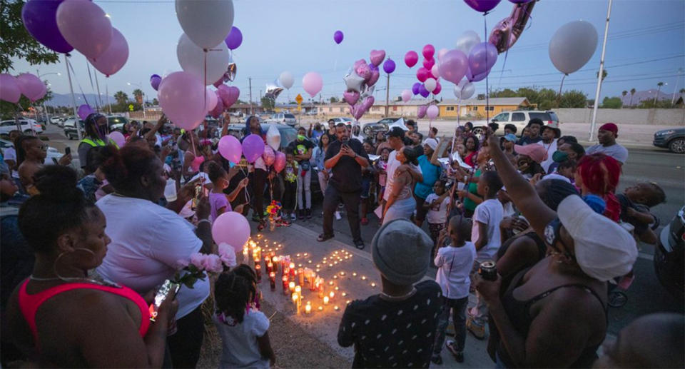 A crowd of people hold balloons around lit candles to remember one-year-old Sayah Deal.