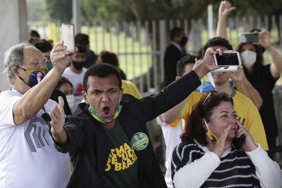 En esta imagen, tomada el 25 de mayo de 2020, partidarios del presidente de Brasil, Jair Bolsonaro, algunos con mascarilla por la pandemia del coronavirus, gritan insultos a los periodistas tras la salida del dirigente de su residencia oficial, el Palacio de Alvorada, en Brasilia, Brasil. (AP Foto/Eraldo Peres)