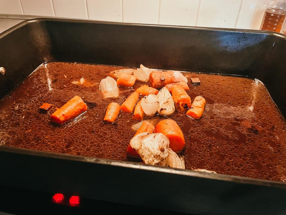 roasting pan with vegetables and meat drippings cooking on a stove