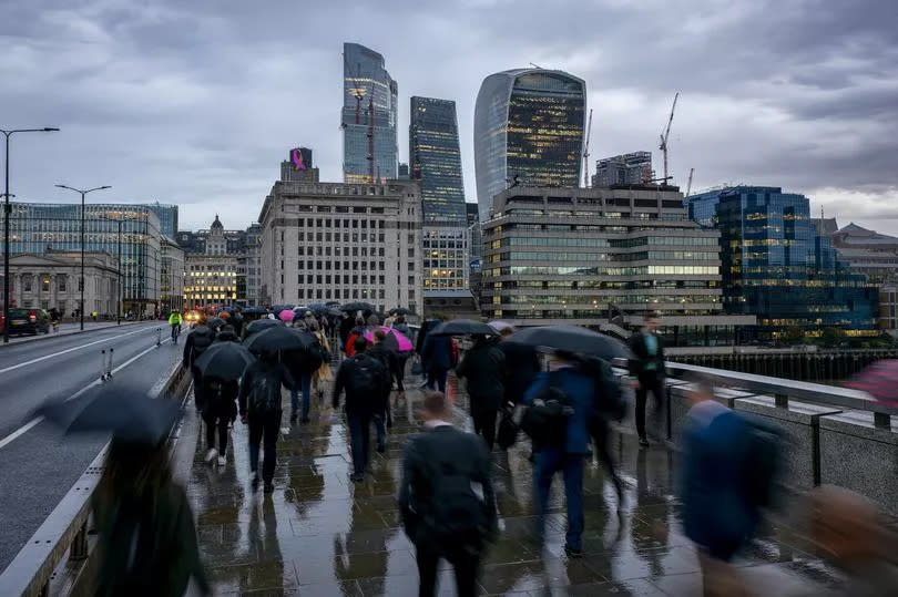 london commuters with umbrellas on a rainy day in front of the city skyline