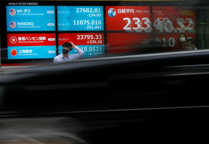 A passersby wearing a protective face mask stands in front of a screen displaying Nikkei share average and world stock indexes, amid the coronavirus disease (COVID-19) outbreak, in Tokyo