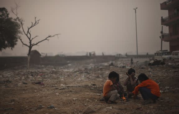 Indian boys sit around a small fire as the morning sun is enveloped by a blanket of smog, Nov. 7, 2012.