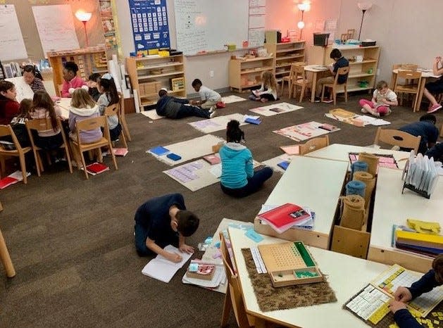 Students in a Lower Elementary classroom - mixed 1st through 3rd grades - is another fundamental of Montessori. The teacher is at the table giving a lesson and the other students are working.
