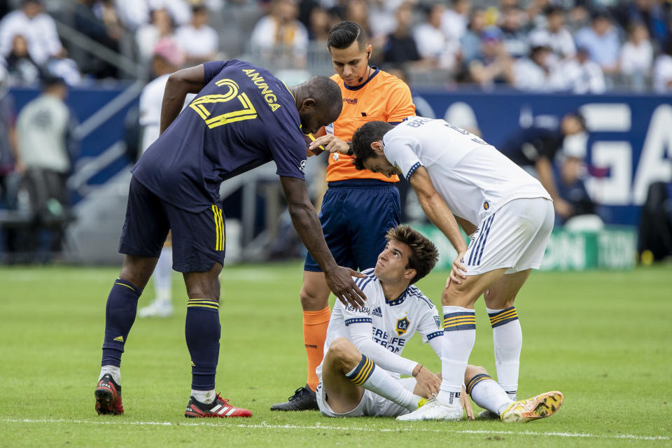 Nashville SC midfielder Brian Anunga, left, extends a hand to LA Galaxy midfielder Riqui Puig, seated center, with midfielder Gaston Brugman, right, watching, after Anunga got a yellow card from referee Armando Villarreal, during the second half of an MLS playoff soccer match, in Carson, Calif., Saturday, Oct. 15, 2022. (AP Photo/Alex Gallardo)