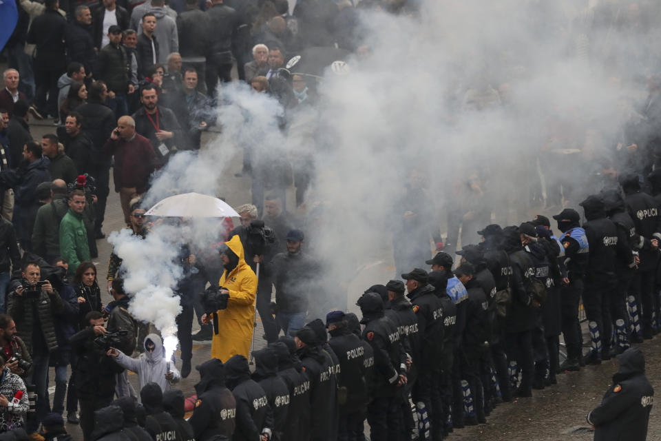 A protester holds a flare as he walks alongside a police formation during an anti-government protest in the capital Tirana, Saturday, April 13, 2019. Albanian opposition parties have returned to the streets for the first time since mid-February calling for the government's resignation and an early election, as the center-right opposition accuses the leftist Socialist Party government of Prime Minister Edi Rama of corruption and links to organized crime, which the government denies. (AP Photo/Hektor Pustina)