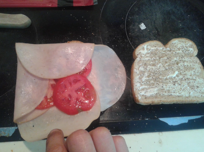 Someone wrapping cold cuts around the tomatoes on a sandwich