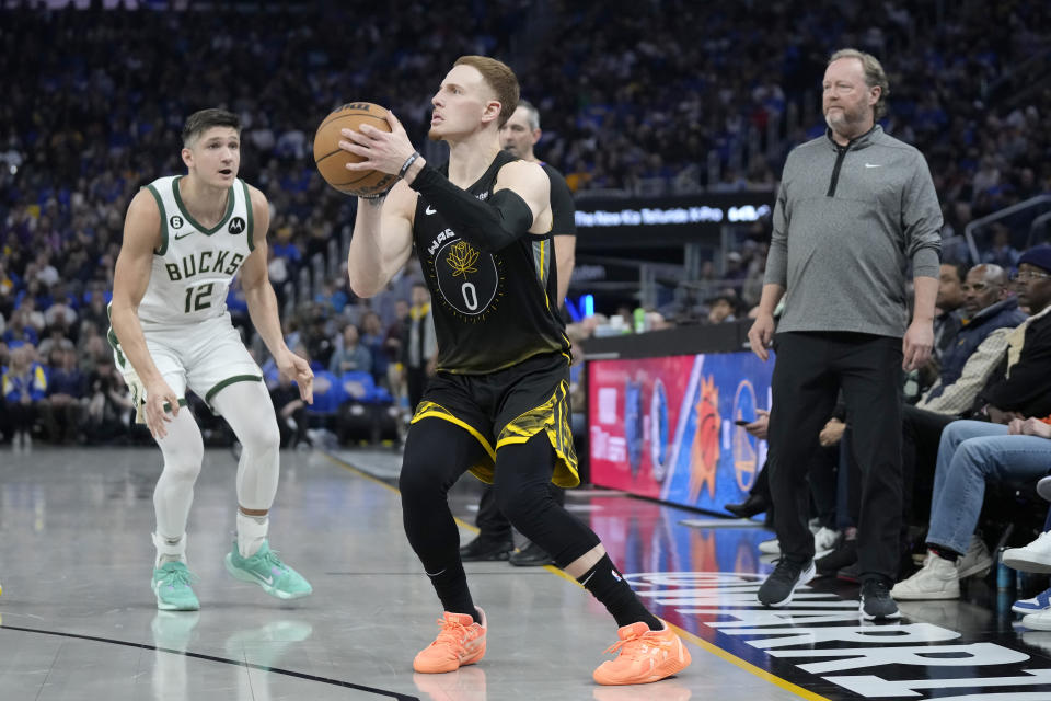 Golden State Warriors guard Donte DiVincenzo (0) shoots a 3-point basket between Milwaukee Bucks guard Grayson Allen (12) and head coach Mike Budenholzer, right, during the first half of an NBA basketball game in San Francisco, Saturday, March 11, 2023. (AP Photo/Jeff Chiu)