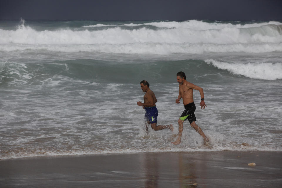 Men run on a public beach during cold weather in the southern port city of Sidon, Lebanon, Wednesday, Jan. 19, 2022. A snowstorm in the Middle East has left many Lebanese and Syrians scrambling to find ways to survive. Some are burning old clothes, plastic and other hazardous materials to keep warm as temperatures plummet and poverty soars. (AP Photo/Mohammed Zaatari)