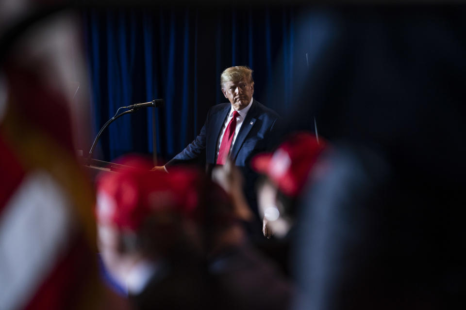 Donald Trump at a podium behind a few out-of-focus MAGA hats.