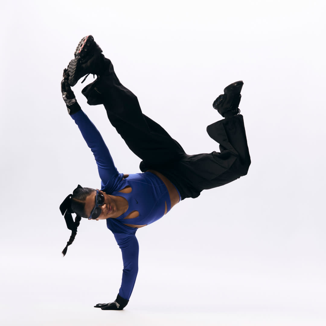  A breakdancer performs a skill while wearing baggy pants and a crop top. 