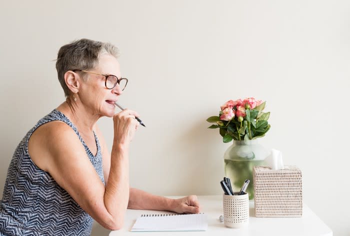 Woman sitting at a desk with a pen in her mouth, thinking about what to write.