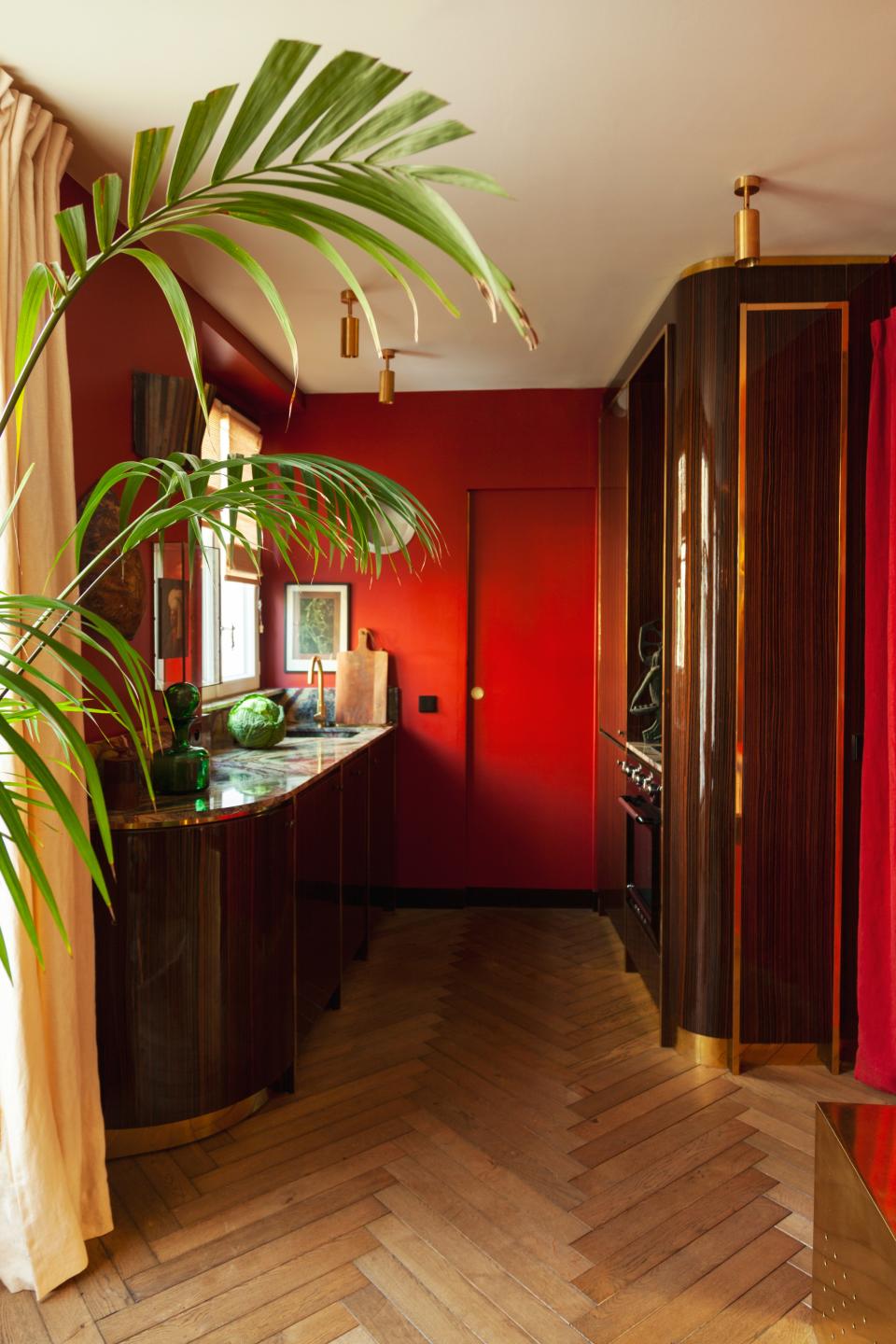 In the kitchen, the red color and lacquered wood give the feeling of being on a train or in a boat. The wall lighting fixture was designed by Hugo Toro and the curtains are by Silva Créations.