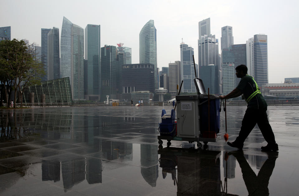 A cleaner passes the city skyline after a morning shower in Singapore April 12, 2016. REUTERS/Edgar Su 