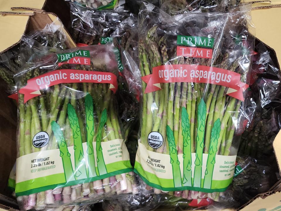 Two bags of Prime Time organic asparagus in see-through bags with red labels in a bin at Costco