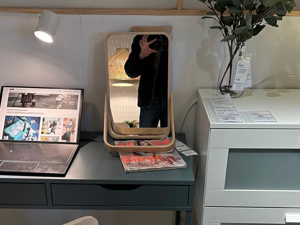 A small mirror on a desk with the writer taking a picture in reflection