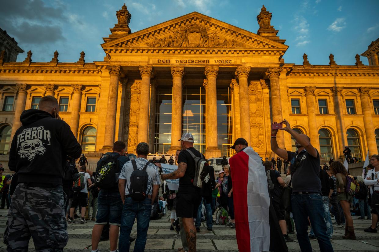 A demonstrator wrapped in a flag of the German empire stands opposite riot policemen standing guard in front of the Reichstag building, which houses the Bundestag lower house of parliament, after protesters tried to storm it at the end of a demonstration called by far-right and COVID-19 deniers to protest against restrictions related to the new coronavirus pandemic, in Berlin, on August 29, 2020. (Photo by John MACDOUGALL / AFP) (Photo by JOHN MACDOUGALL/AFP via Getty Images)