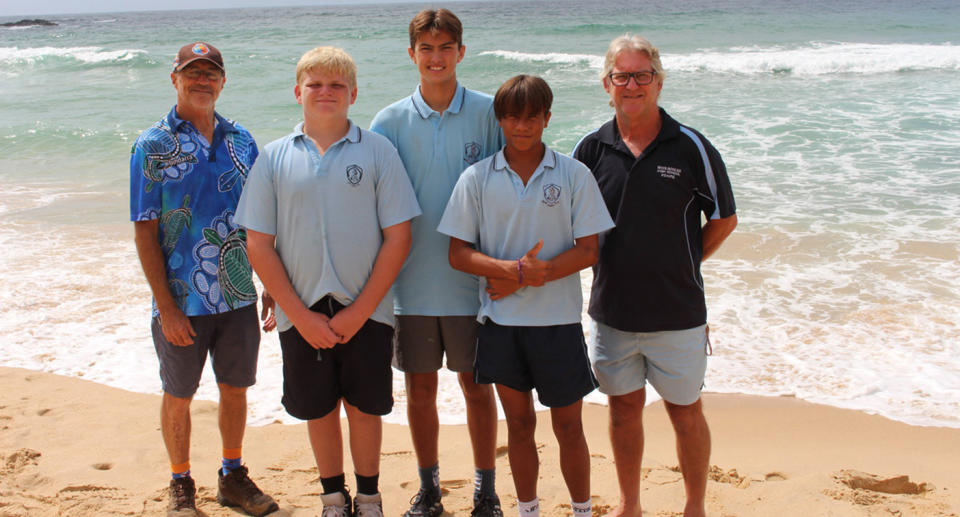 John Elliott (teacher), Koby Kudrins, Finn Casper, Jack Hayes and John Morgan (teacher) stand on the sand at Woolgoolga Back Beach