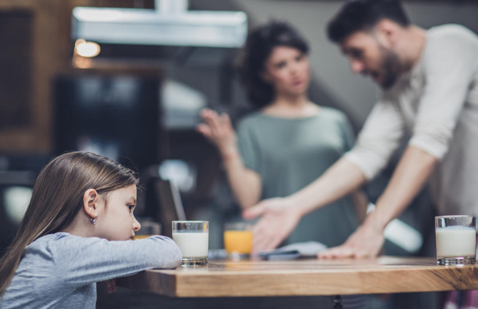 Little girl feeling sad while her parents are arguing in the background.